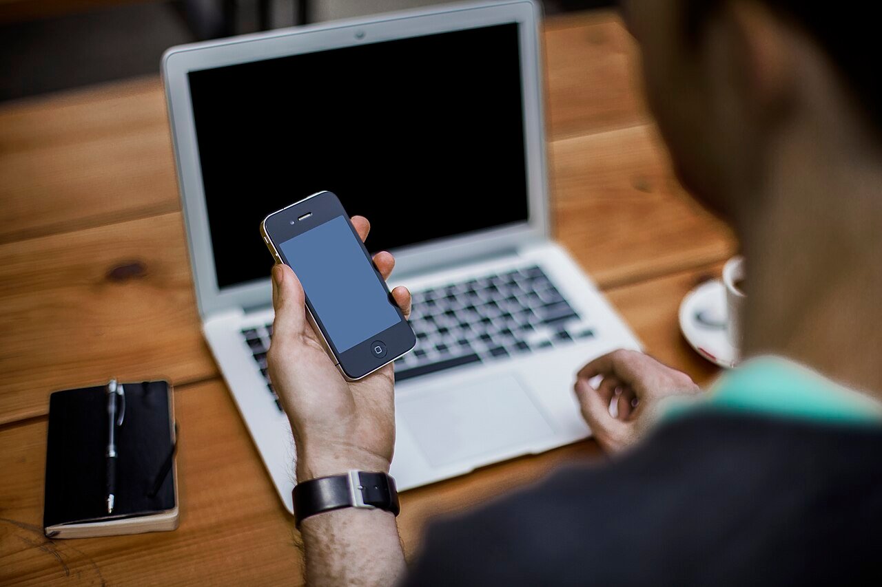 Customer holding a smartphone in front of a laptop at a polished desk setup